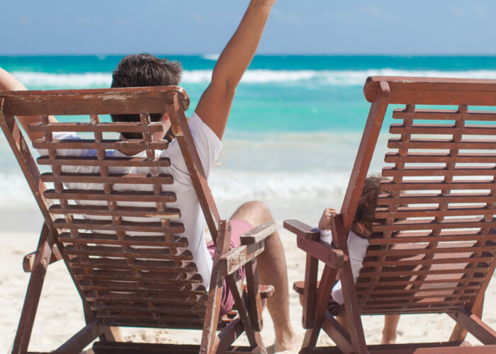 An image of a man and his sone sitting in Adirondack chairs on the beach