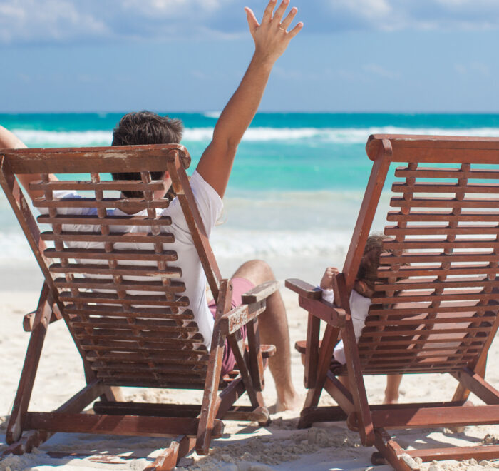 An image of a man and his sone sitting in Adirondack chairs on the beach