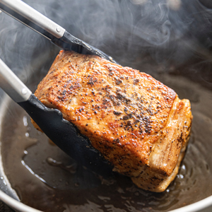 An image of someone pan searing a seasoned filet of salmon