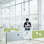 An image of a man standing in front of the windows of an office building