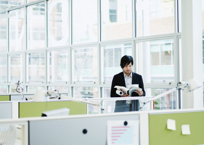 An image of a man standing in front of the windows of an office building