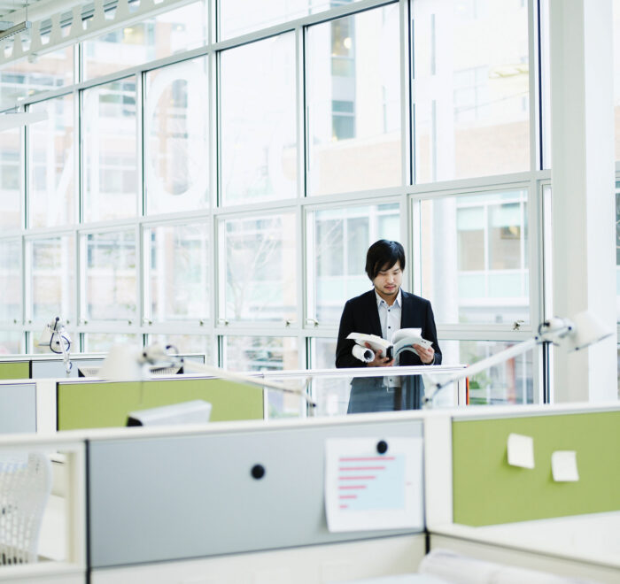 An image of a man standing in front of the windows of an office building