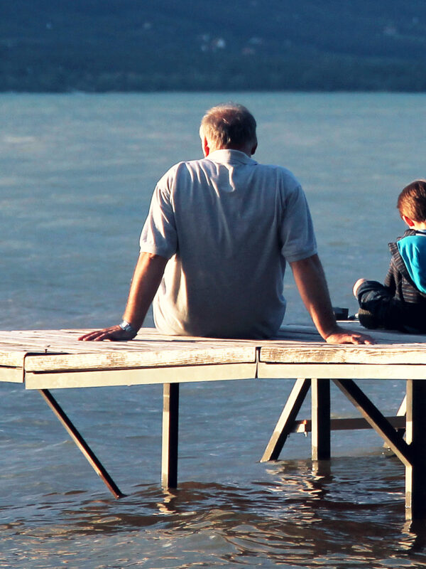 An image of a grandfather and his grandson sitting on a wooden dock at the lake