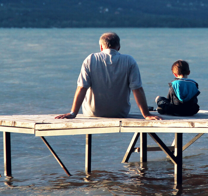 An image of a grandfather and his grandson sitting on a wooden dock at the lake